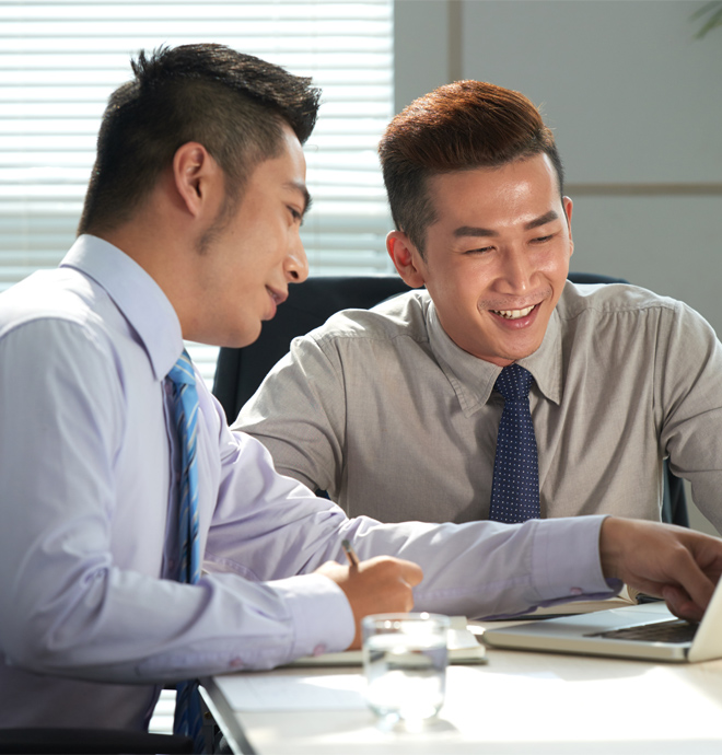 two man at a table smiling at a laptop