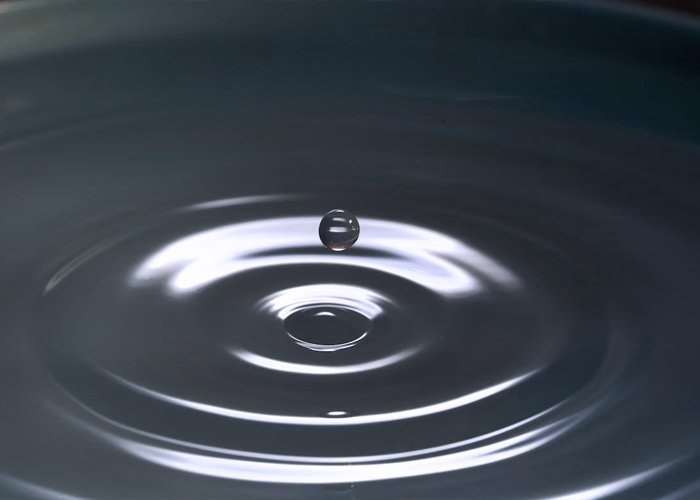 a water droplet dropping into a pool of water causing a ripple